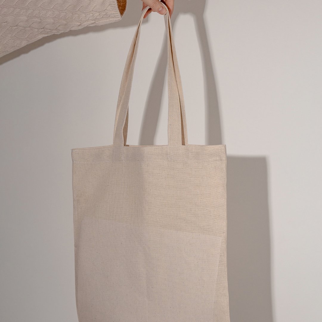 Hand holding a natural canvas tote bag against a neutral background, eco-friendly reusable bag by Wellaine.