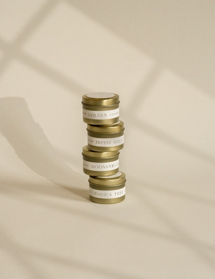 Four Orchid & Ash mini candle tins stacked under natural light with artistic shadows.