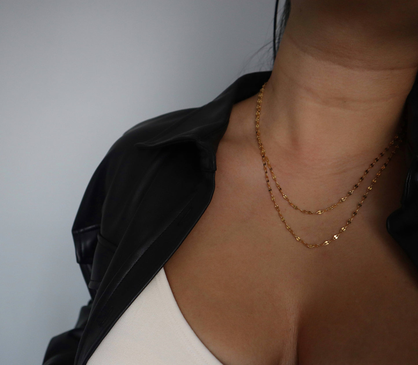 Layered styling of the JESSA Jewelry Lia Chain with another gold chain over a low-cut top and black jacket.