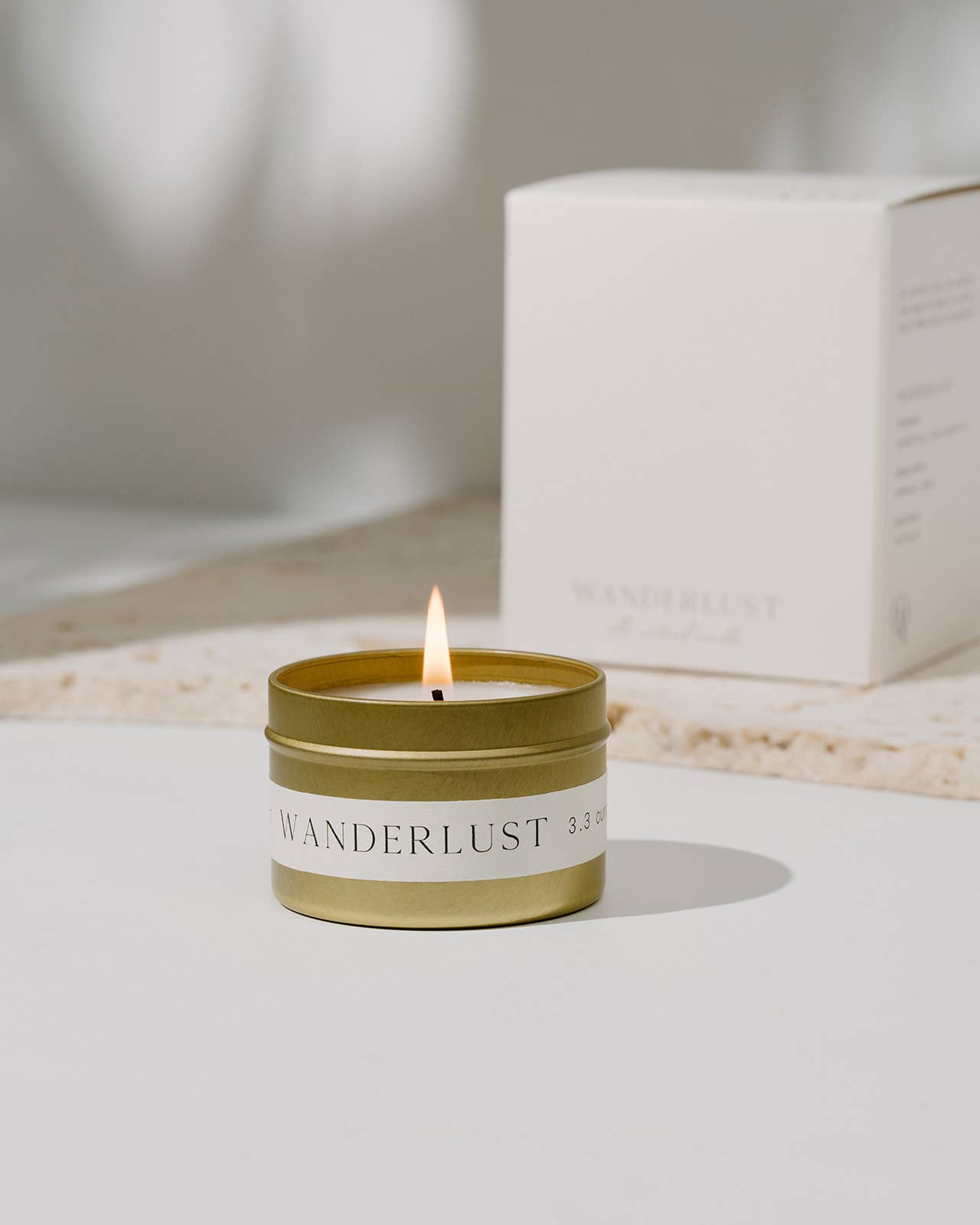 Gold tin Wanderlust candle with box in warm natural light by Orchid & Ash.