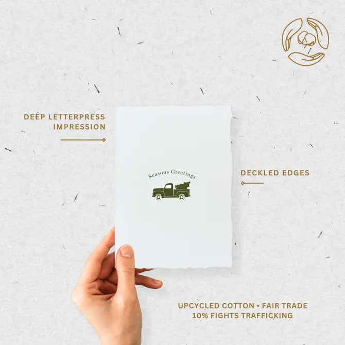 Hand holding eco-friendly holiday card highlighting deep letterpress impression, deckled edges, and fair-trade cotton paper.