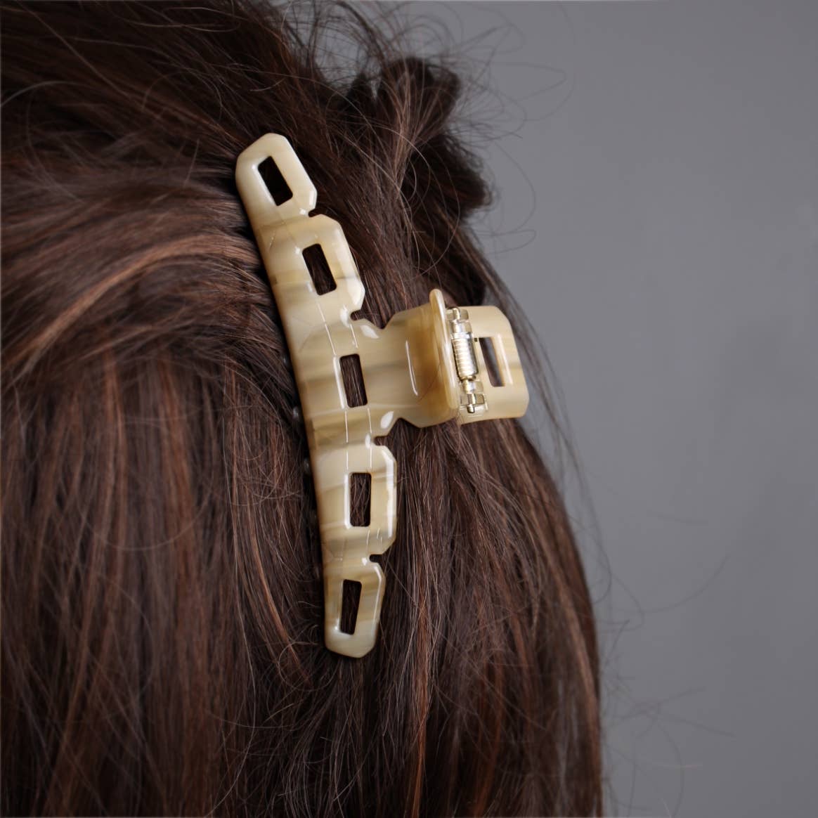 Side-back view of cream oat colored French claw clip by Peignée Paris holding brunette hair up.