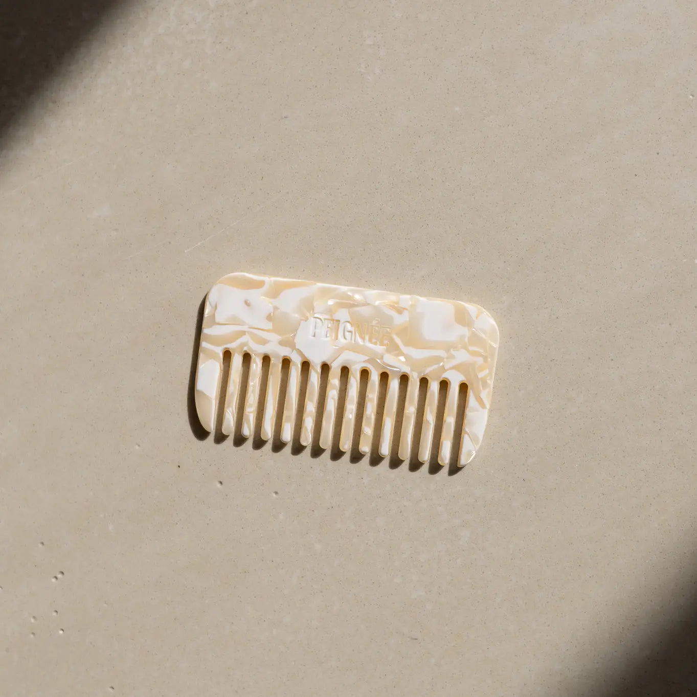 Peignée Paris wide-tooth comb in ivory marble finish resting on stone surface.