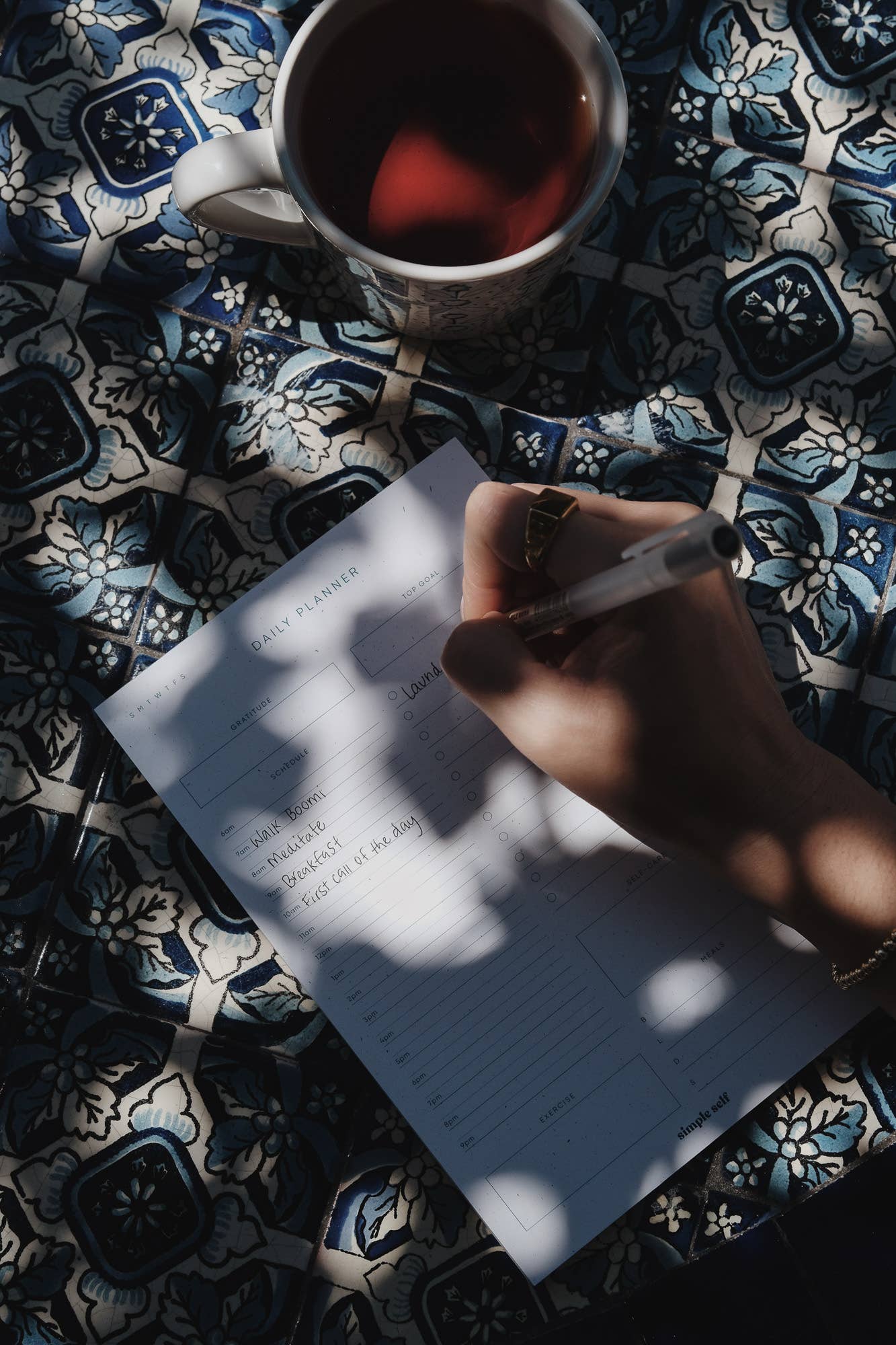 Person writing in the Simple Self Daily Planner Notepad, focusing on gratitude and daily schedule sections.