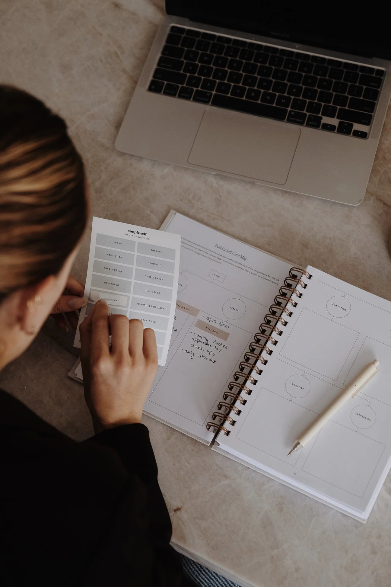 Overhead view of a person using various sticker sets in a Simple Self Co planner next to a laptop.