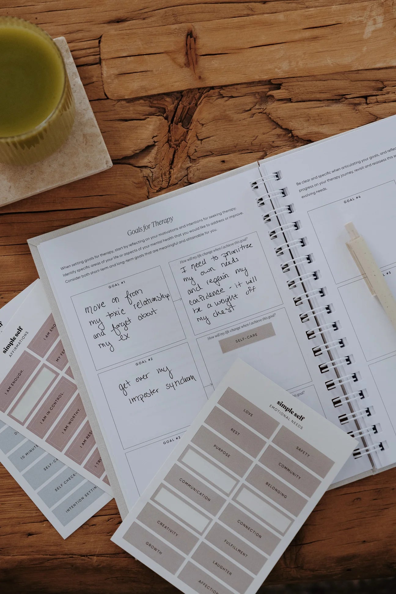 Sticker Sets by Simple Self Co beside an open guided journal on a wooden table.