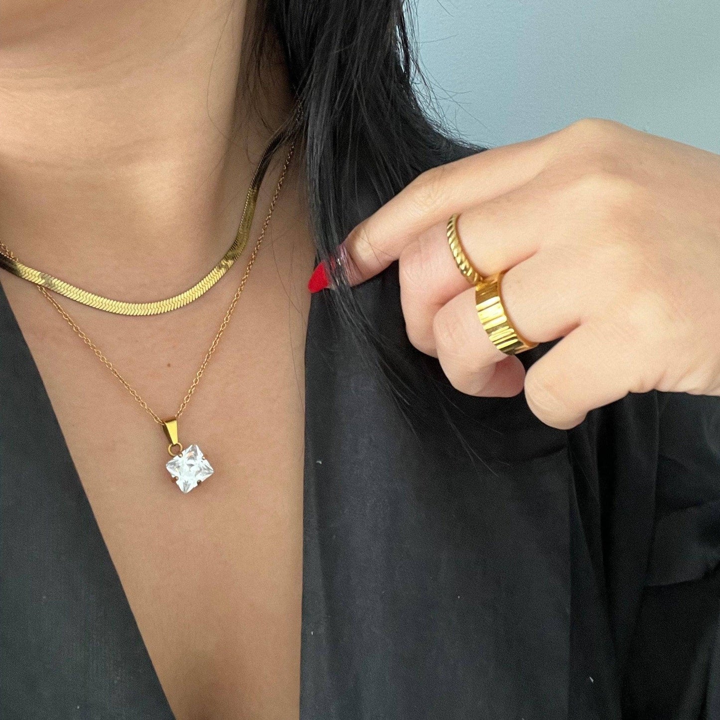 Woman layering gold snake chain with gold pendant necklace and gold rings.