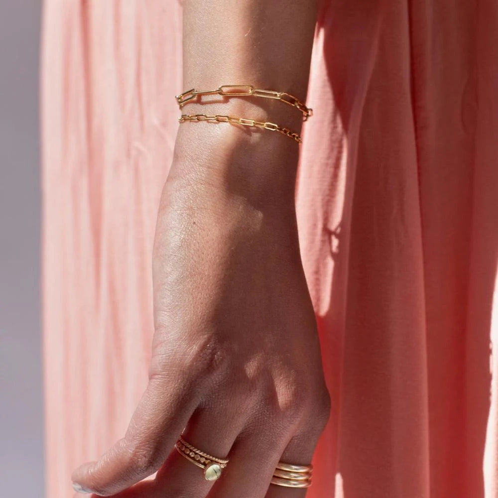 Token Jewelry Narrow Links Bracelet in gold on wrist, photographed in light with rings.