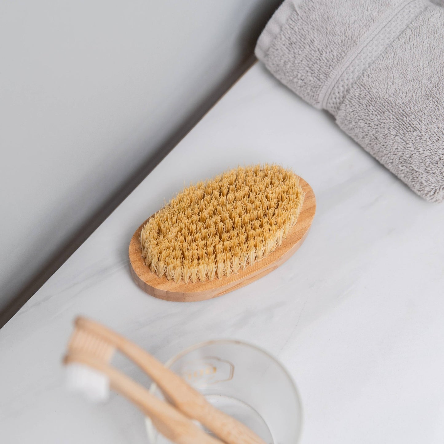 Detoxifying dry body brush styled on clean white marble with towel and bath accessories, luxury self-care routine.