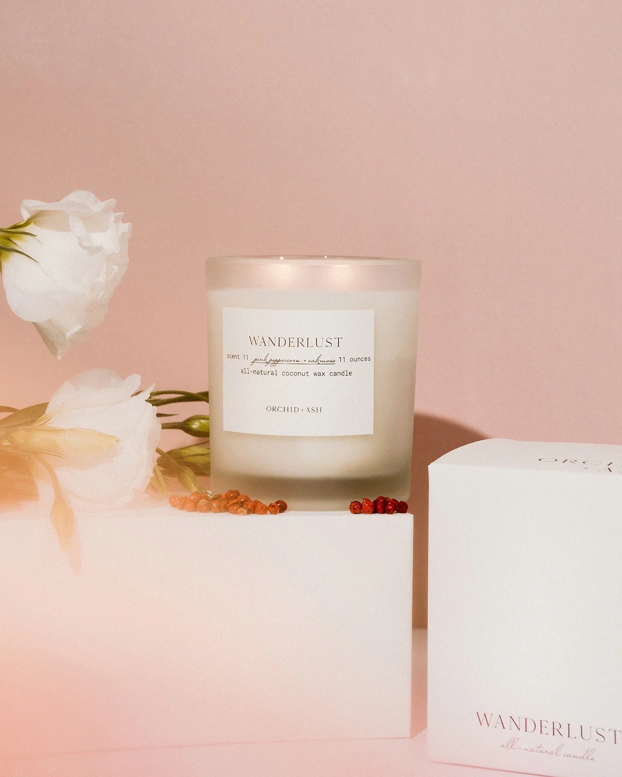 Orchid & Ash Wanderlust candle styled with flowers and gift boxes on a romantic pink background.