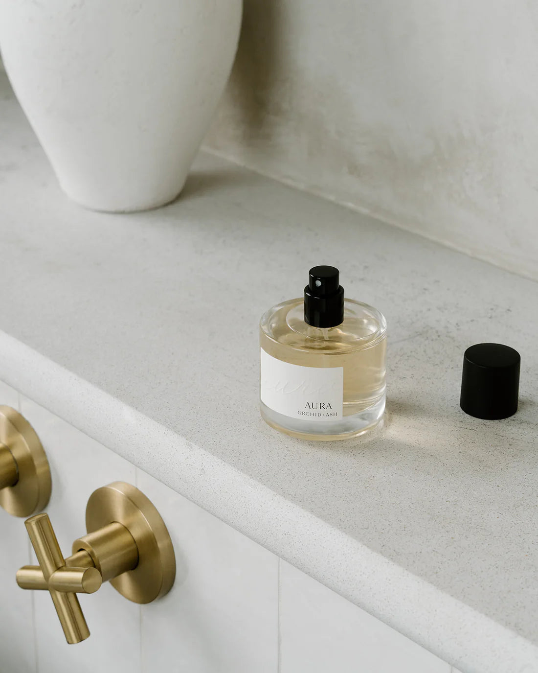Aura perfume by Orchid & Ash on a minimalist bathroom counter with brass faucet and black cap off.