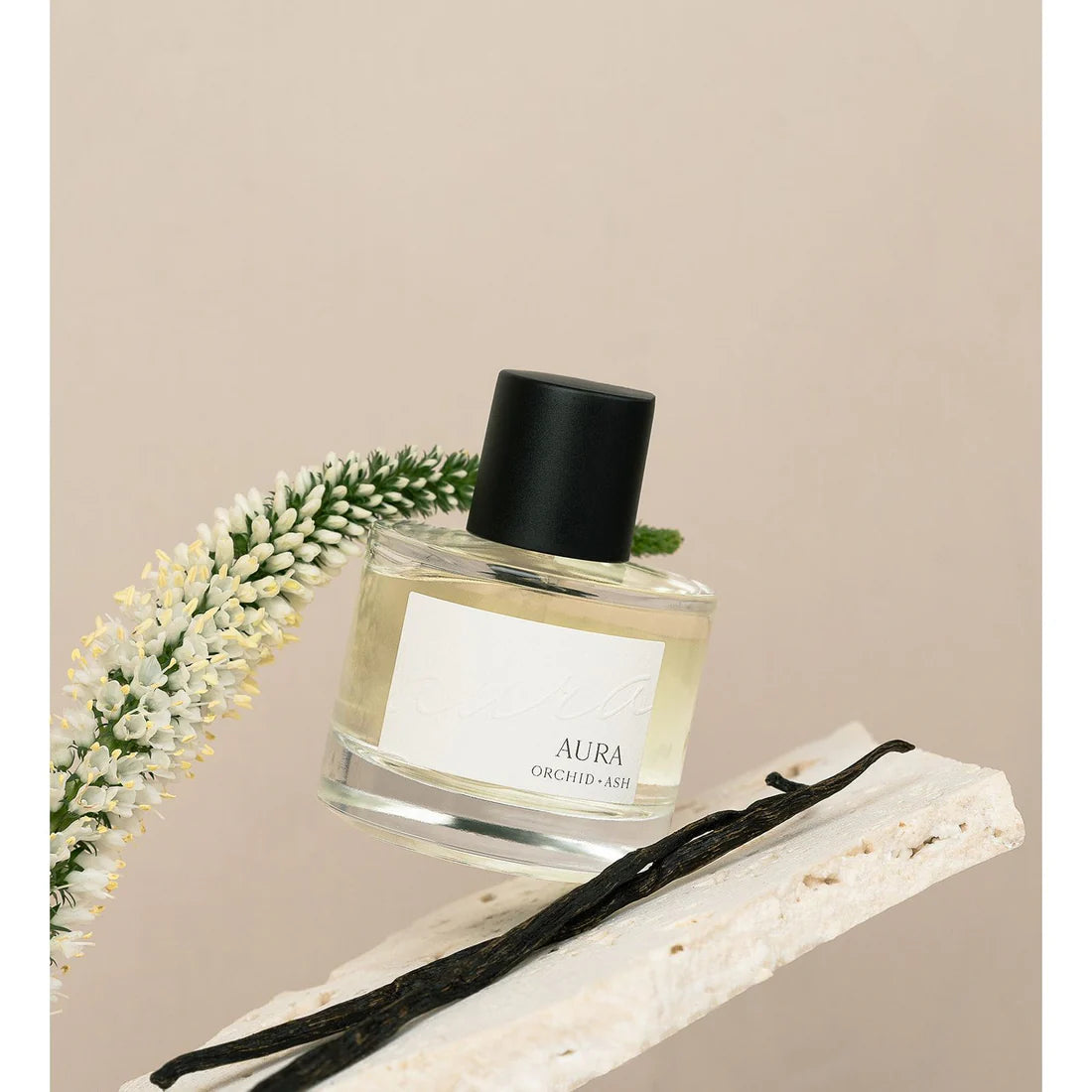 Aura perfume by Orchid & Ash surrounded by white flowers and a vanilla bean on a neutral background.