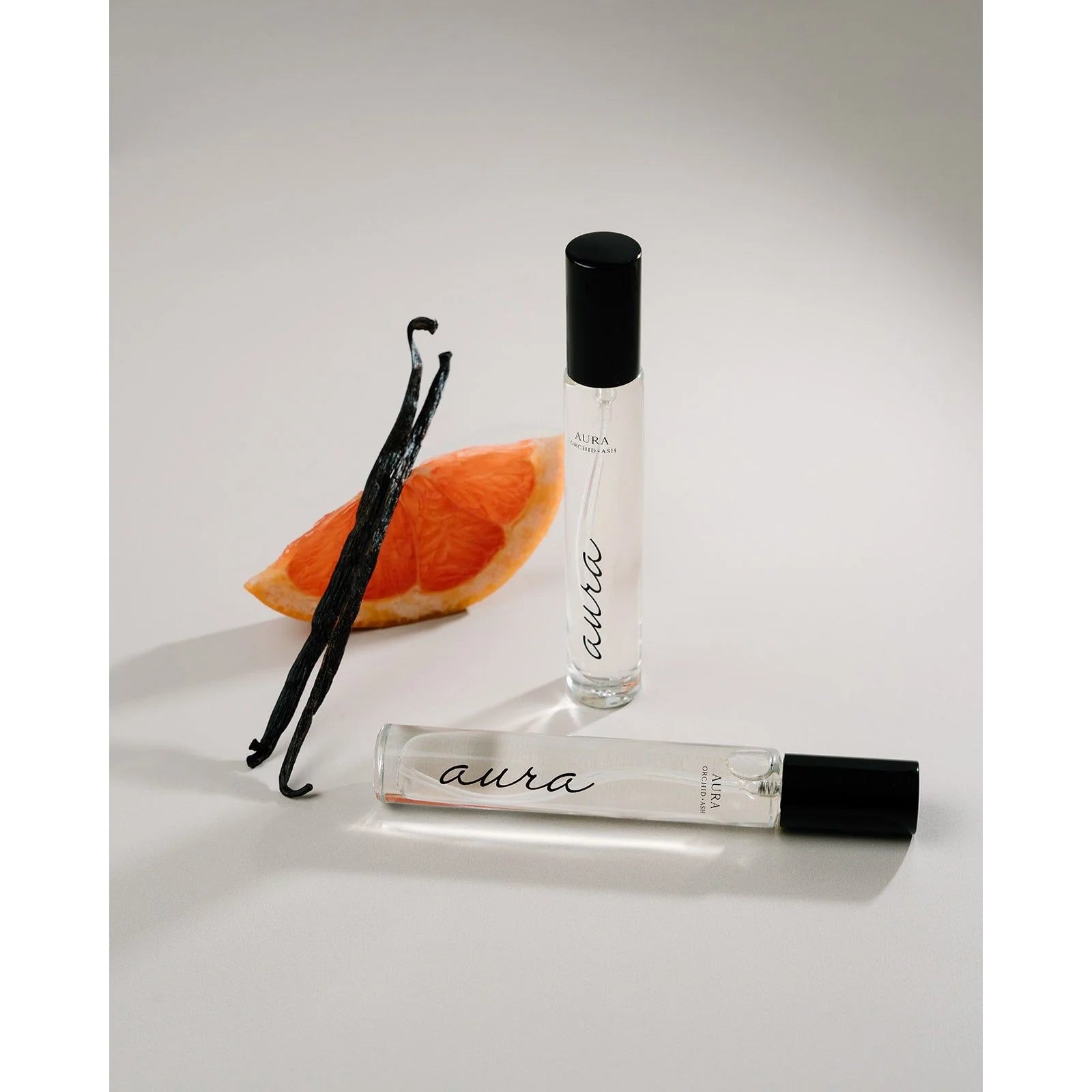 Aura travel spray by Orchid & Ash standing next to grapefruit and vanilla bean on white background.