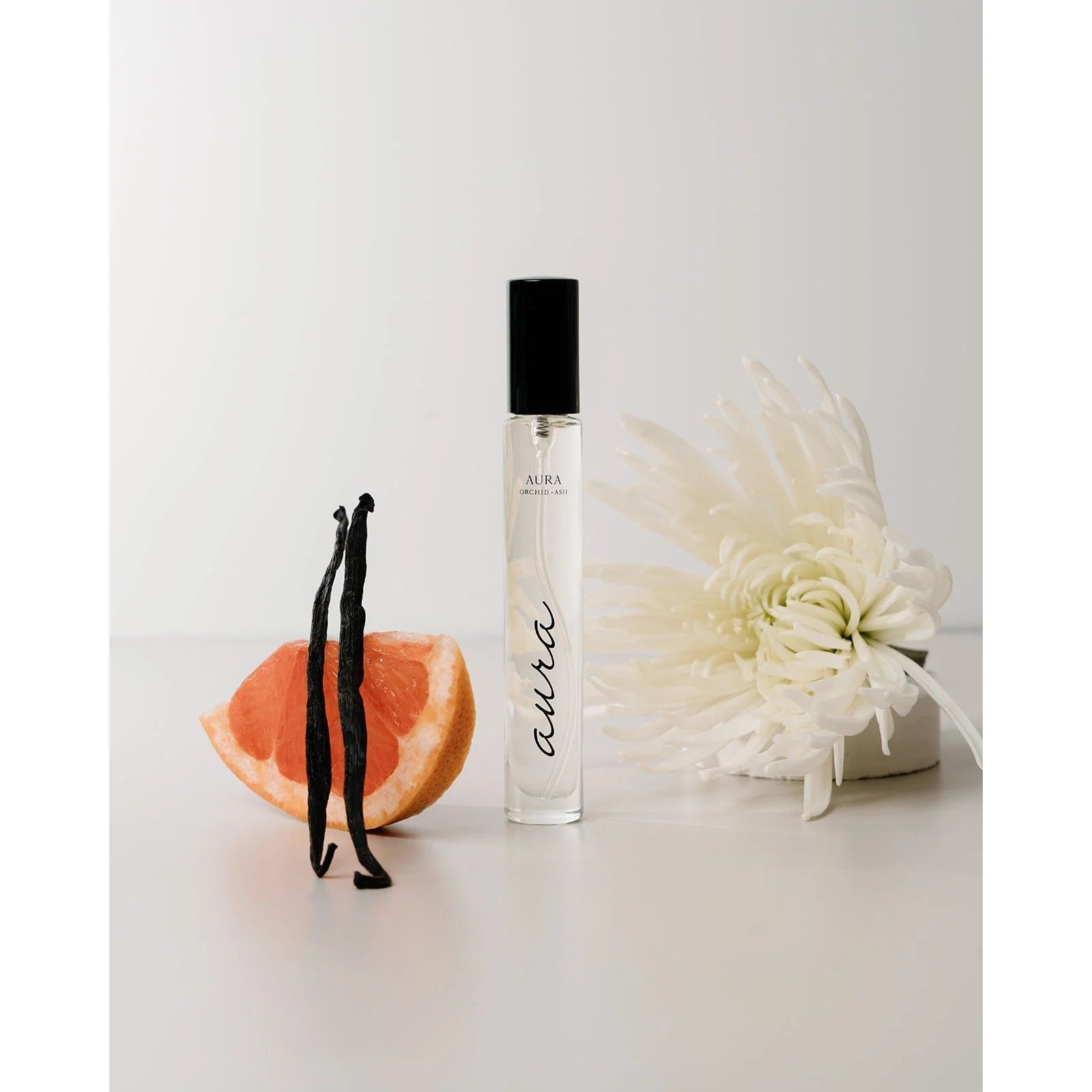 Aura spray by Orchid & Ash placed beside a grapefruit wedge, vanilla bean, and cream-colored flower.