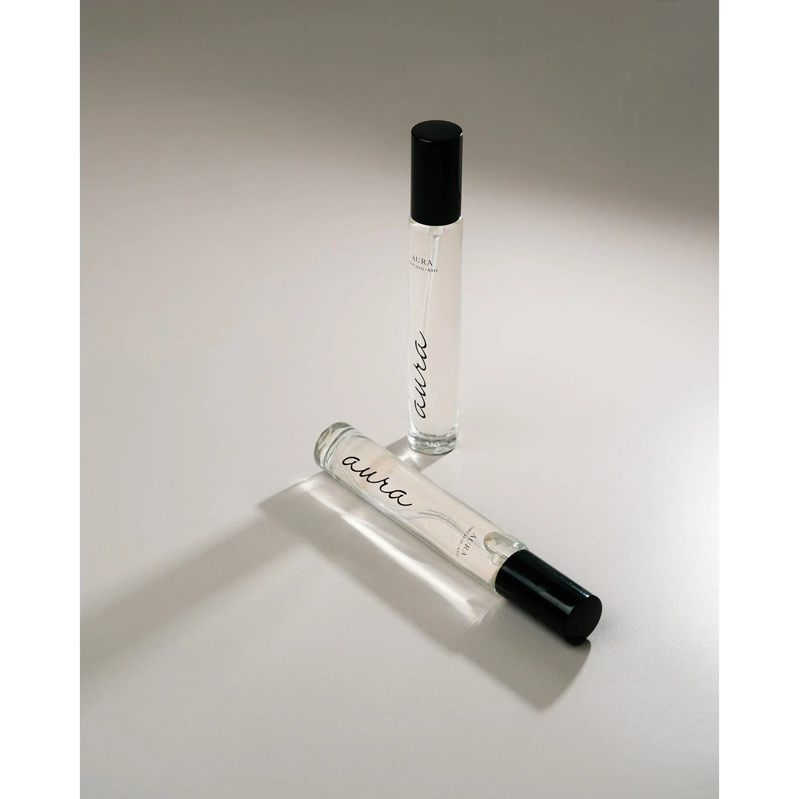 Pair of Aura travel spray perfumes by Orchid & Ash laying on a white surface.
