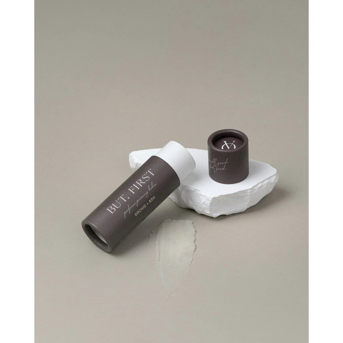 But First solid perfume balm resting on a white stone slab, cap placed beside it.