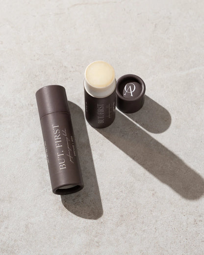 Open tube of But First solid perfume balm by Orchid & Ash casting a soft shadow on a stone surface.