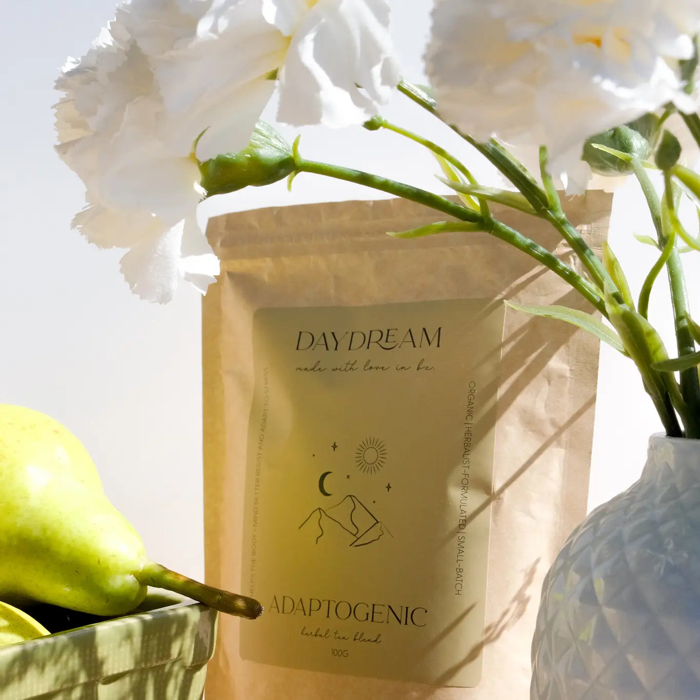 Daydream Organics Adaptogenic Herbal Tea pouch displayed on a wooden table beside a vase of flowers.