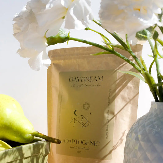Daydream Organics Adaptogenic Herbal Tea pouch displayed on a wooden table beside a vase of flowers.