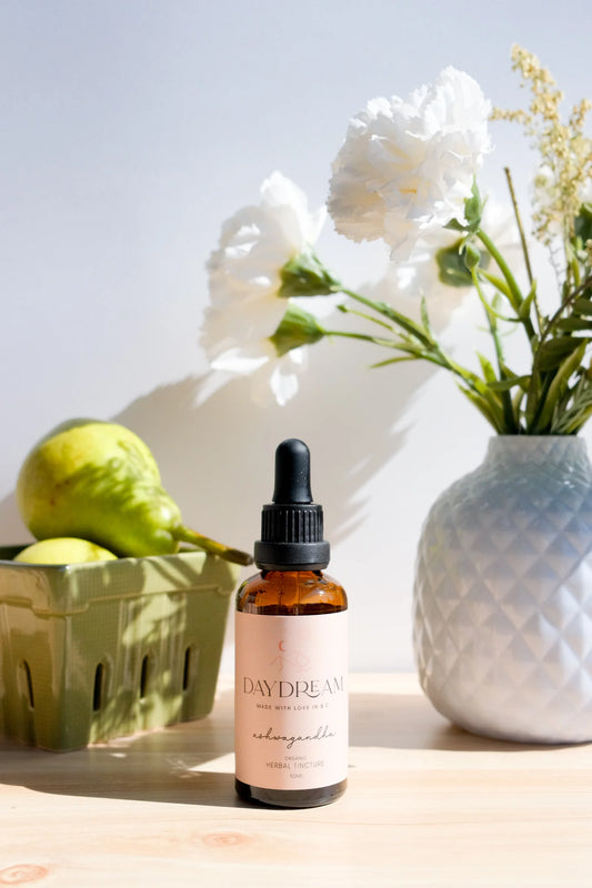 Daydream Organics Ashwagandha Herbal Tincture placed on a wooden table with a vase with flowers and pear fruit in the background.