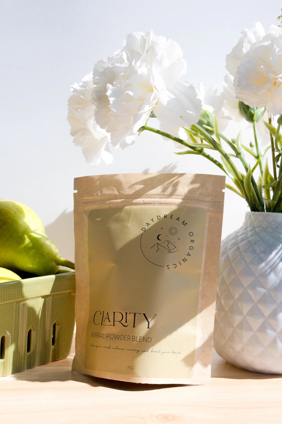 Daydream Organics Clarity Herbal Powder Blend displayed on a table with pears and a vase of flowers.