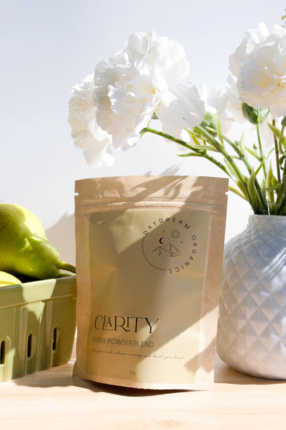 Daydream Organics Clarity Herbal Powder Blend displayed on a table with pears and a vase of flowers.