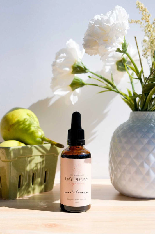 Sweet Dreams Tincture by Daydream Organics resting on a table with fresh flowers and pears