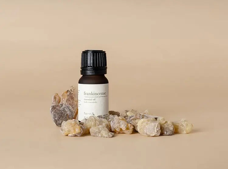 Fern & Petal Frankincense Essential Oil bottle surrounded by frankincense resin pieces on a neutral background.