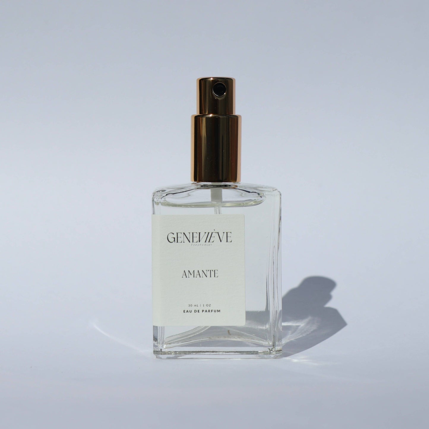 Closed bottle of Genevieve Fragrances Amante perfume with gold spray top on white background.