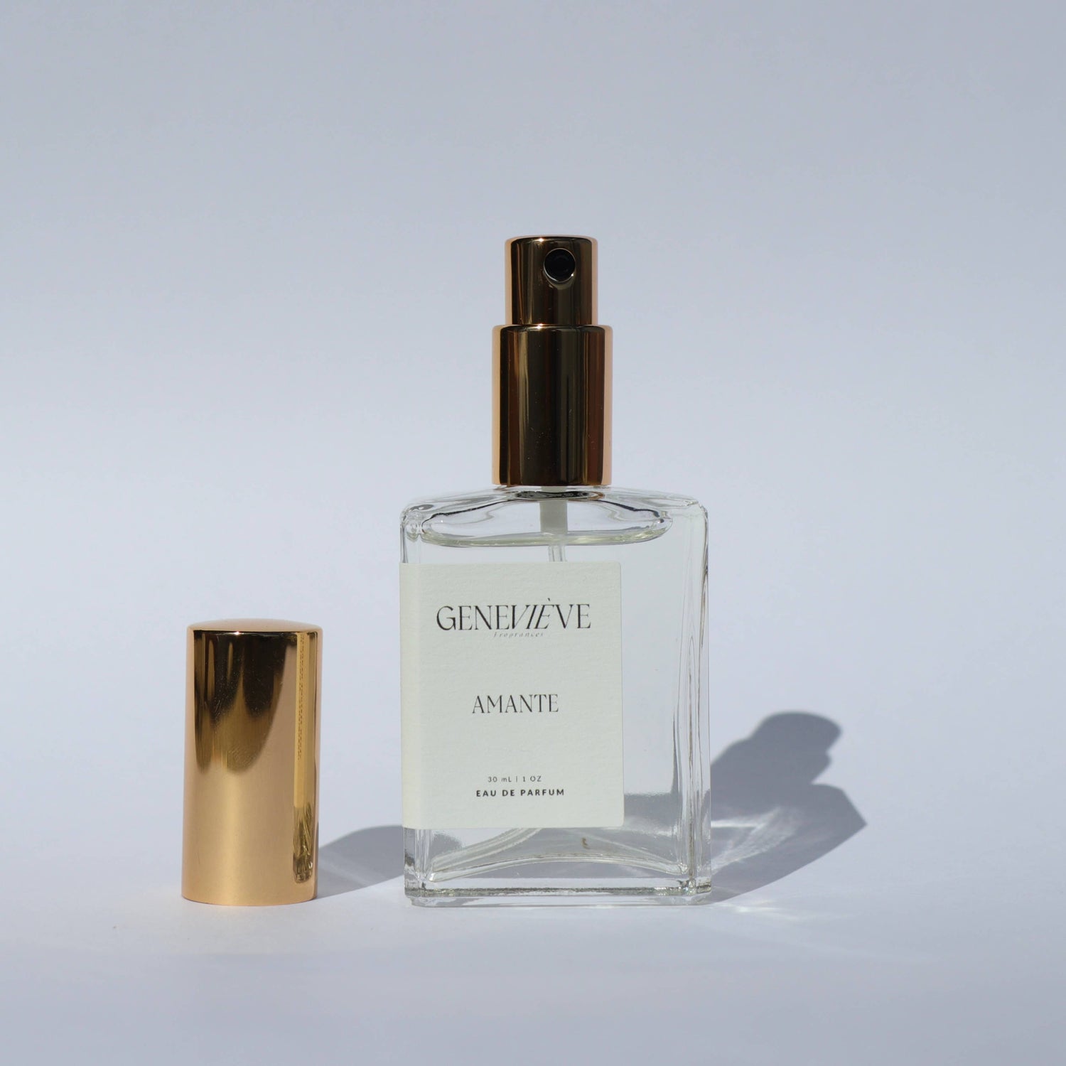 Open bottle of Genevieve Fragrances Amante perfume with gold cap on white background.
