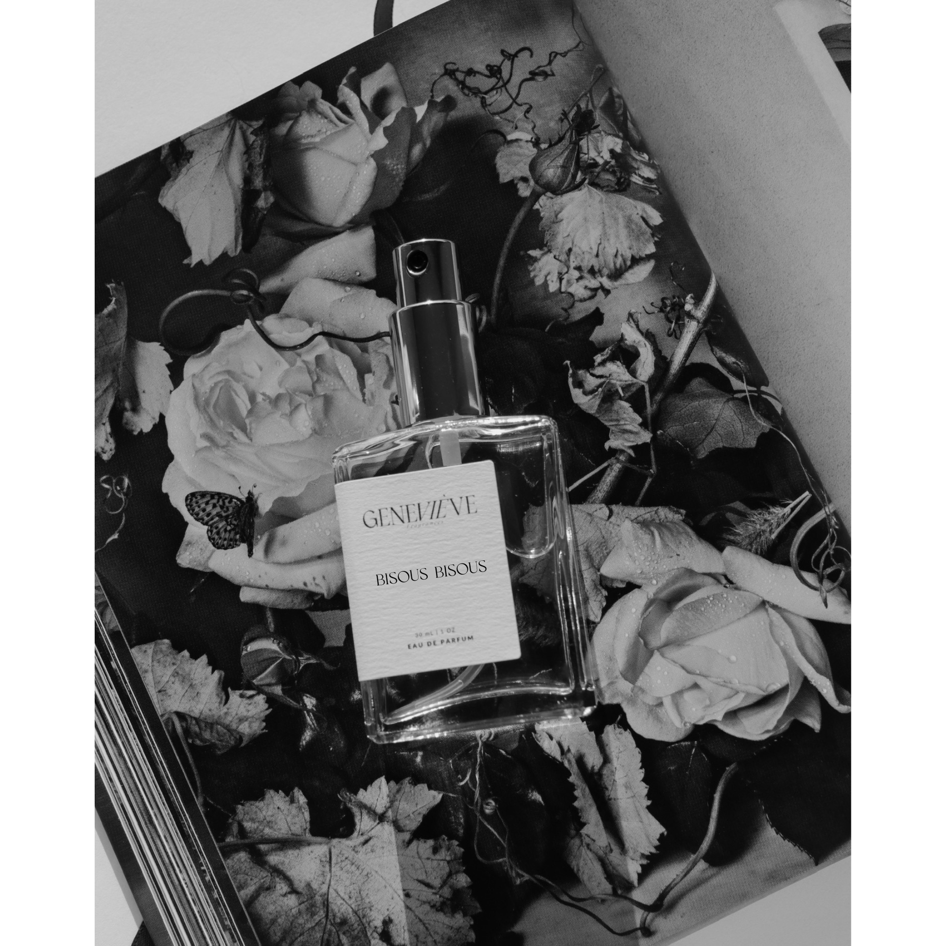 Genevieve Fragrances Bisous Bisous perfume bottle resting on a black-and-white floral magazine spread.