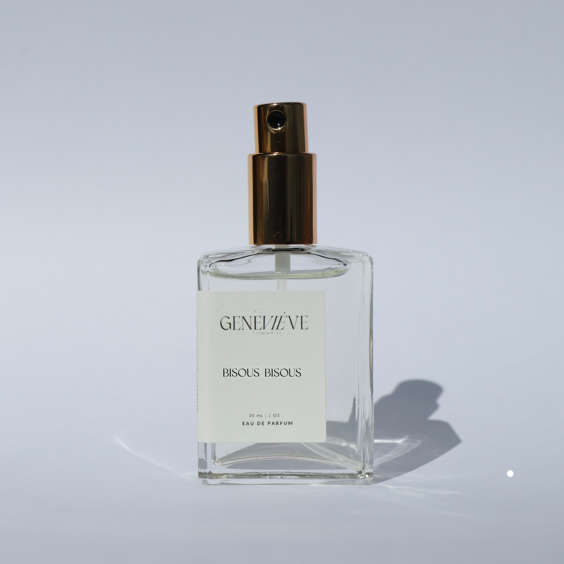 Closed bottle of Genevieve Fragrances Bisous Bisous perfume with open gold spray top on white background.