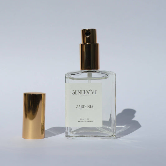 Open bottle of Genevieve Fragrances Gardenia perfume with gold cap on white background.