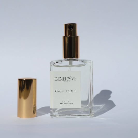Open bottle of Genevieve Fragrances Orchid Noire perfume with gold cap on white background.