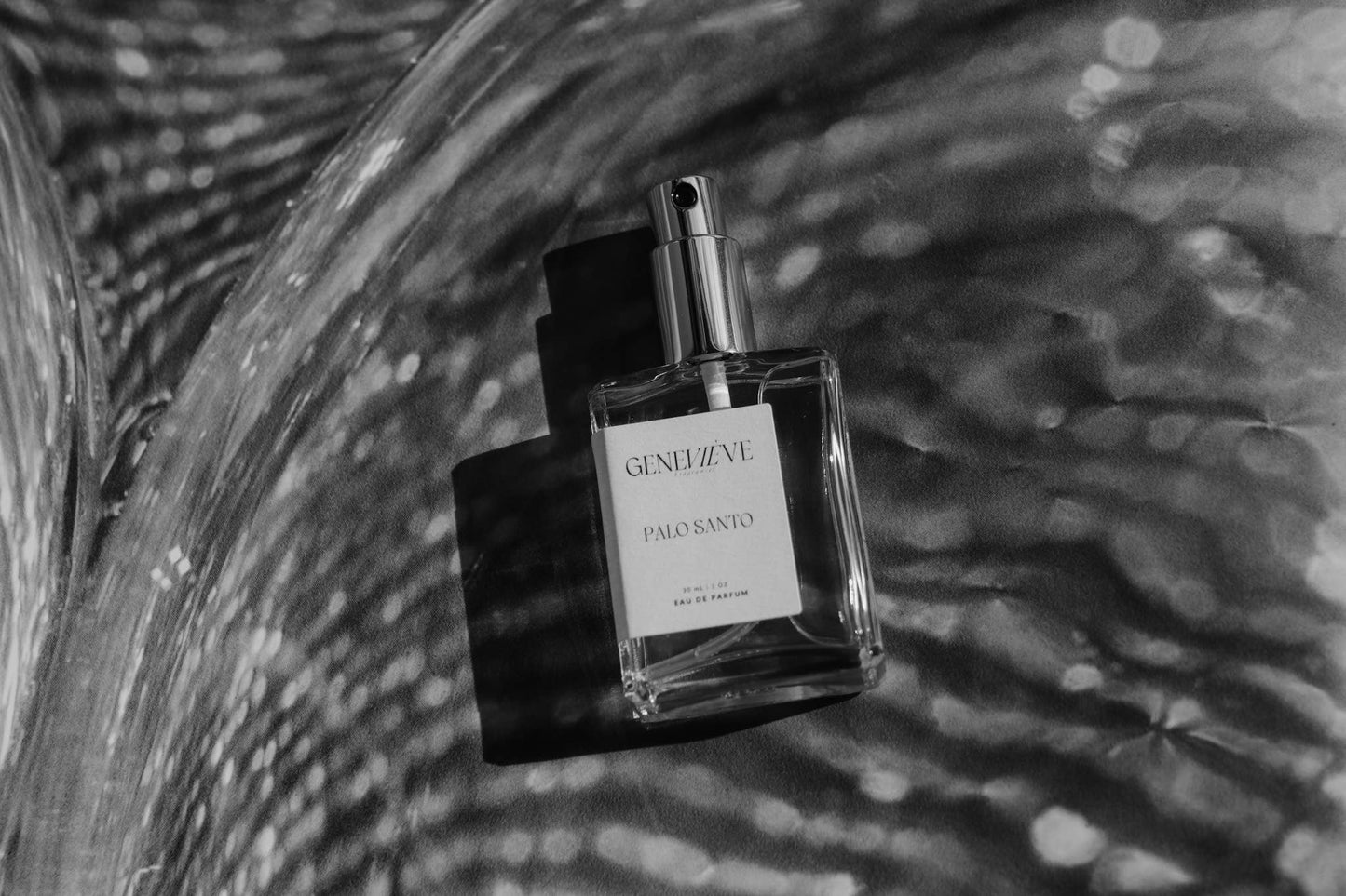 Artistic black and white photo of Geneviève Palo Santo Eau de Parfum bottle against a textured, wavy background.