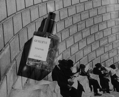 Artistic black and white photo of Geneviève Toujours Eau de Parfum bottle against a brick wall with shadows.