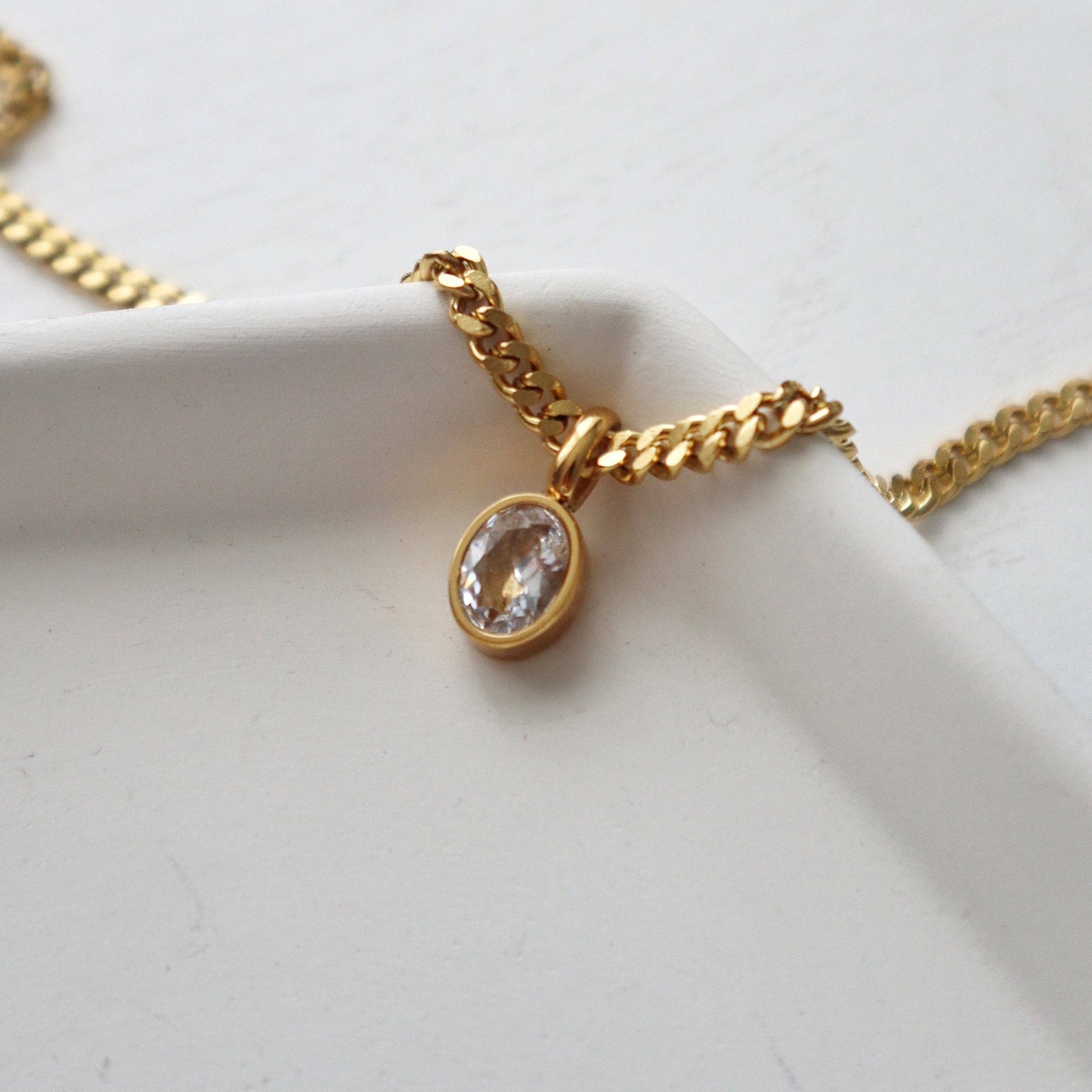 Close-up of CZ gem pendant and chain from JESSA Jewelry on white ceramic dish.