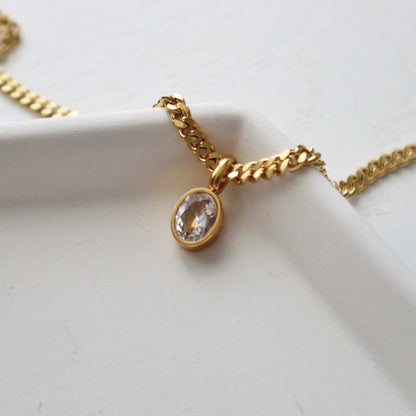 Close-up of CZ gem pendant and chain from JESSA Jewelry on white ceramic dish.