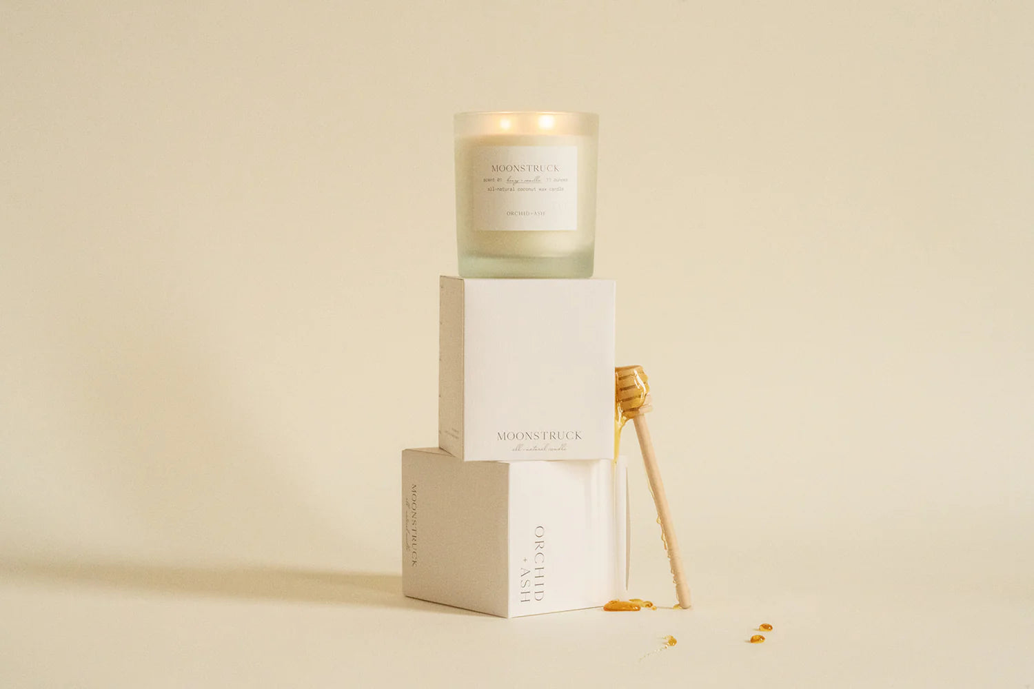 Moonstruck frosted glass candle and boxes showcasing packaging, elevated on stacked plinths with delicate dried florals and dripping honey comb wand.