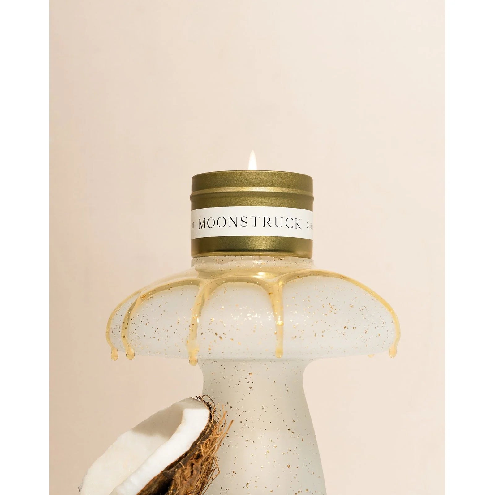 Gold Orchid & Ash Moonstruck candle tin burning on a spotted ceramic mushroom shaped pedestal with coconut and honey details.