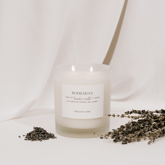 Orchid & Ash Bohemian double-wick candle burning in a frosted glass jar with scattered lavender.