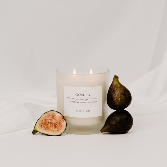 Orchid & Ash Golden candle with sliced figs on a white sheet background.