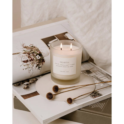 Hearth glass double-wick candle by Orchid & Ash lit on top of a magazine book stack, styled with dried flowers.