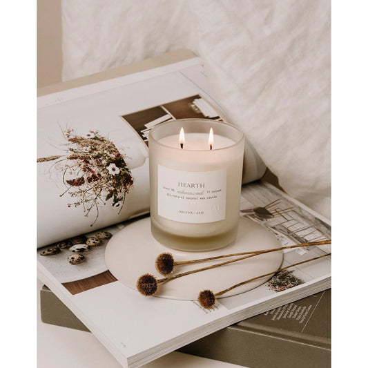 Hearth glass double-wick candle by Orchid & Ash lit on top of a magazine book stack, styled with dried flowers.