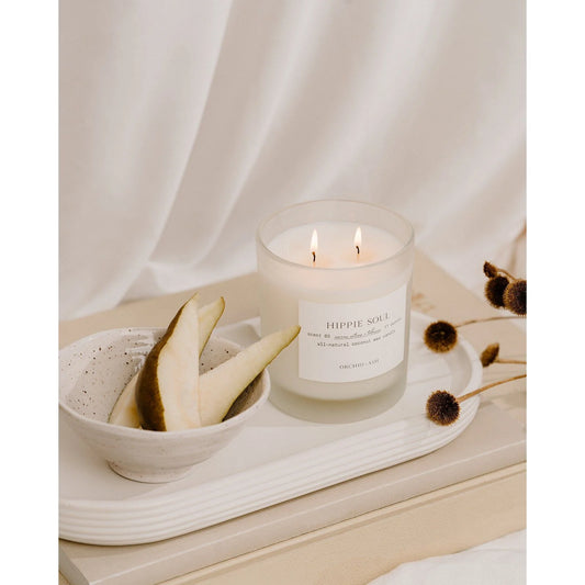 Orchid & Ash Hippie Soul glass candle lit on ceramic tray with sliced pear and dried botanicals.
