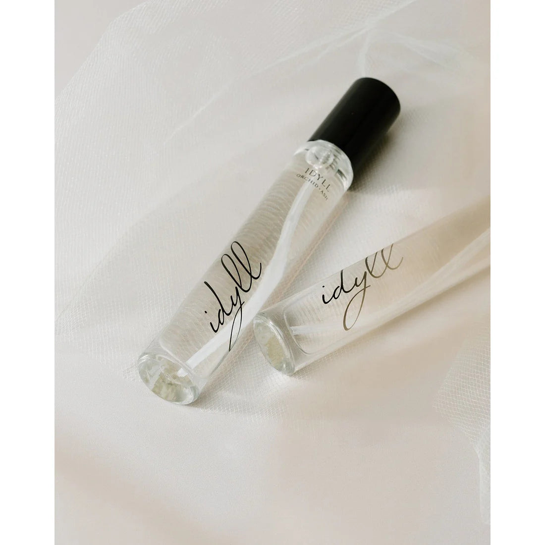 Two Idyll travel size perfumes by Orchid & Ash styled on white chiffon with soft natural lighting.