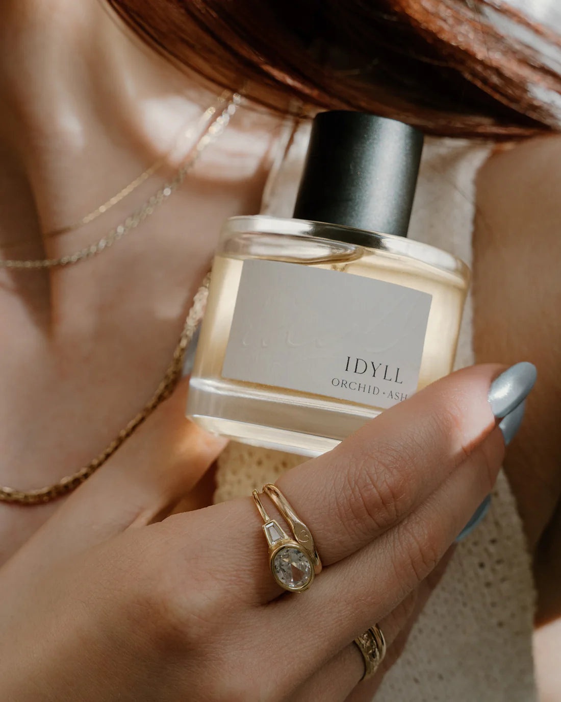  Idyll perfume bottle by Orchid & Ash held close to the chest with layered gold jewelry.
