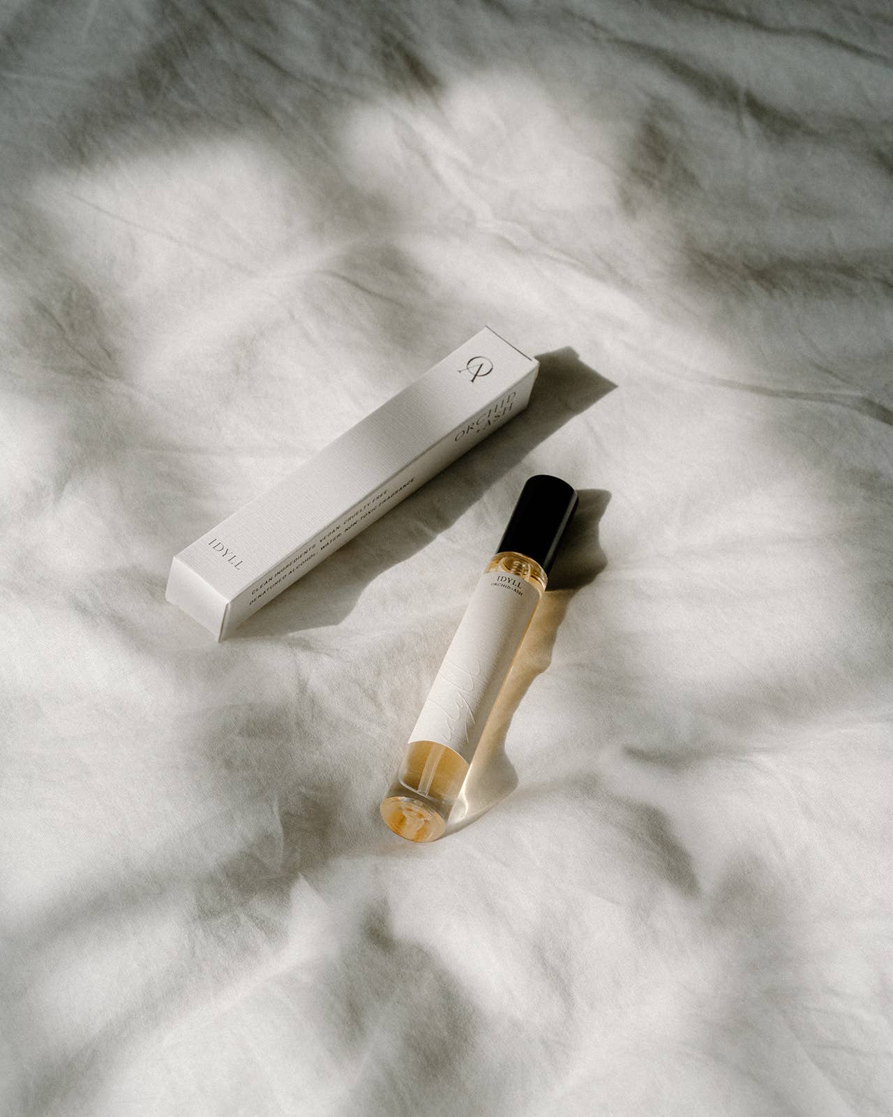 Idyll roller perfume and its box by Orchid & Ash placed on softly wrinkled white linen.