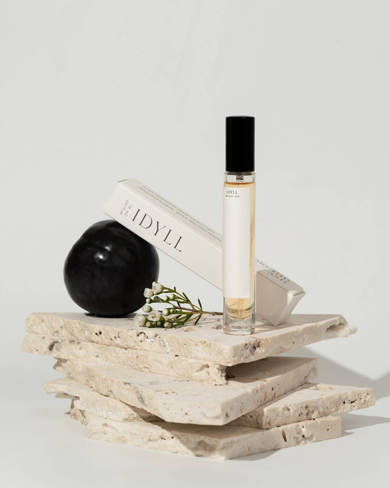 Idyll perfume travel spray by Orchid & Ash styled with box and black plum on stacked stone tiles.