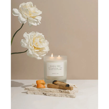 Orchid & Ash Joshua Tree candle on white pedestal stone pieces, with white flowers, burnt palo santo and orange peel skin.